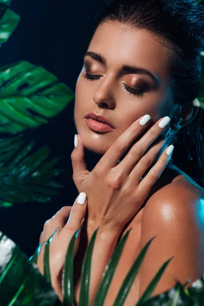 Selective focus of young naked woman touching face near fresh green leaves — Stock Photo