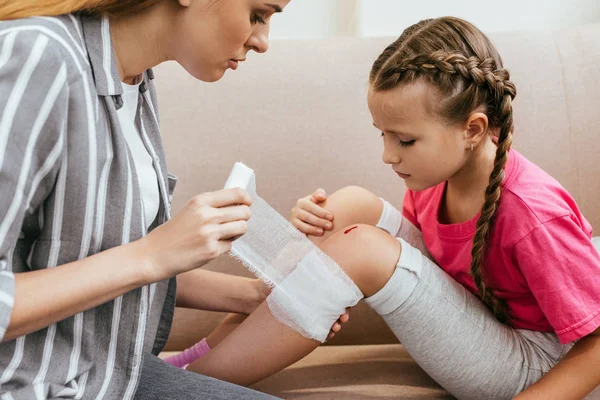 Beautiful mother wounding bandage around knee of daughter — Stock Photo