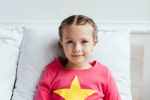 Adorable child sitting on bed and looking at camera — Stock Photo