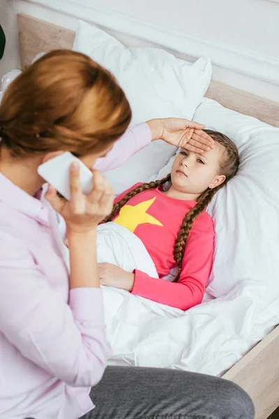 Besorgte Mutter bei Online-Beratung, während sie Stirn kranker Tochter mit Fieber berührt — Stockfoto