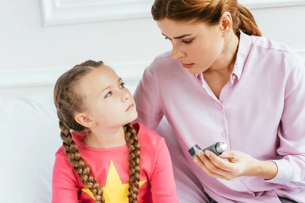 Беспокойная мать дает ингалятор грустной дочери с астмой — стоковое фото