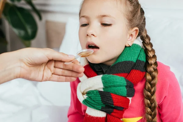 Mère donnant sirop à fille malade avec écharpe au lit — Photo de stock