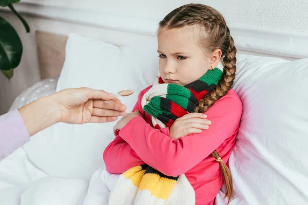 Mother giving syrup to offended ill daughter with scarf in bed — Stock Photo