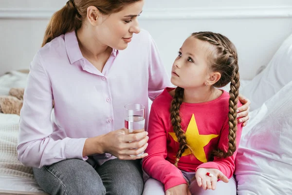 Smiling mother giving glass of water to diseased daughter with pill — Stock Photo