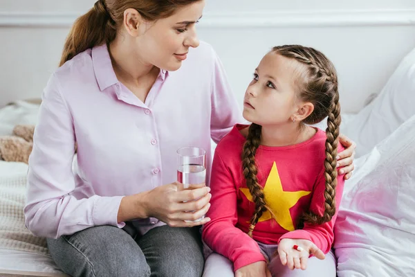 Sonriente madre dando vaso de agua a hija enferma con píldora - foto de stock