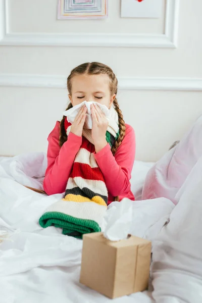 Sick kid with runny nose holding napkins while sitting on bed — Stock Photo