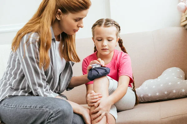 Besorgte Mutter hält Eisbeutel-Kompresse am schmerzhaften Knie ihrer Tochter — Stockfoto