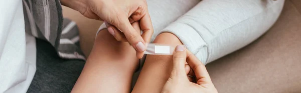 Panoramic shot of mother applying plaster on knee of daughter — Stock Photo