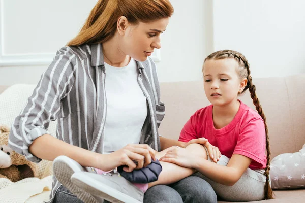 Mother holding ice bag compress on painful knee of emotional daughter — Stock Photo