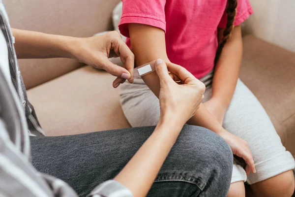 Cropped view of mother applying adhesive bandage on elbow of daughter — Stock Photo