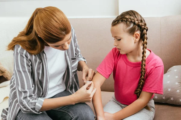 Madre aplicando vendaje adhesivo en el codo de la triste hija - foto de stock