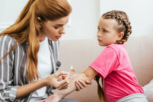 Mère attrayante appliquant un bandage adhésif sur le coude de la fille — Photo de stock