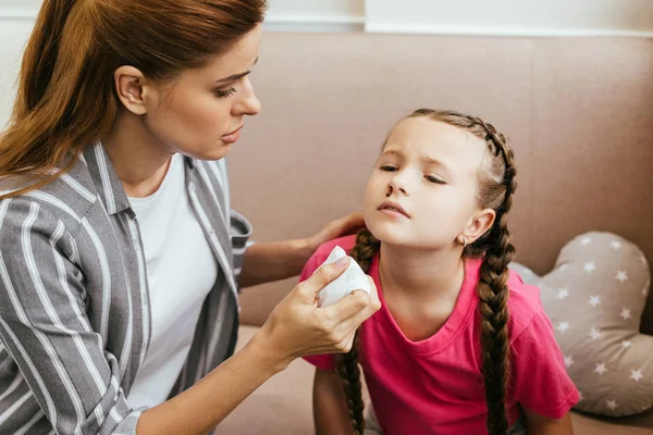 Worried mother holding napkin near daughter with nasal bleeding — Stock Photo