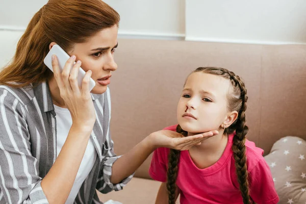 Worried mother having online consultation on smartphone while her daughter having nasal bleeding — Stock Photo