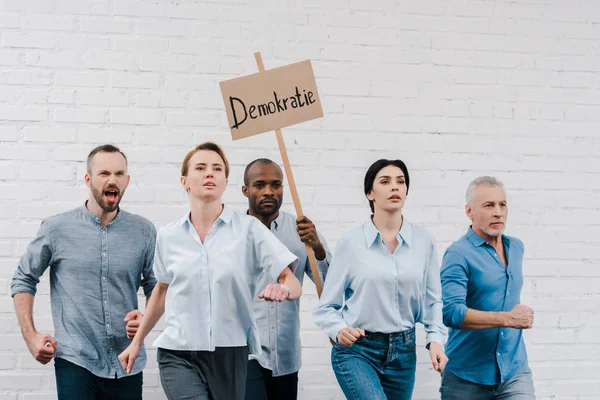 Grupo de personas caminando cerca de hombre afroamericano sosteniendo pancarta con letras demokratie - foto de stock