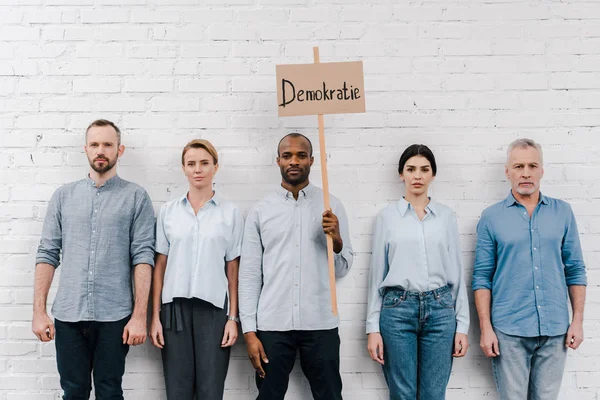 Grupo de pessoas que estão perto de homem afro-americano segurando cartaz com demokratie lettering — Fotografia de Stock