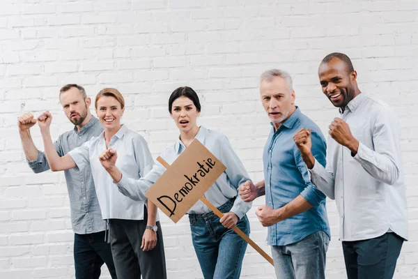 Group of multicultural people standing near woman holding placard with demokratie lettering — Stock Photo