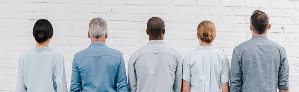 Plano panorámico de personas multiculturales de pie cerca de la pared de ladrillo - foto de stock