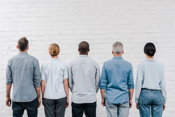 Vista posteriore di persone multiculturali in piedi vicino al muro di mattoni — Foto stock