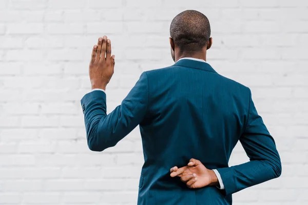 Back view of african american diplomat standing with fingers crossed near brick wall — Stock Photo