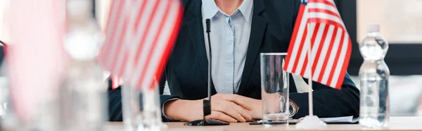 Panoramic shot of businesswoman near american flags on table — Stock Photo