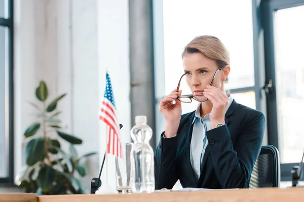 Selective focus of beautiful diplomat wearing eyeglasses near american flag — Stock Photo