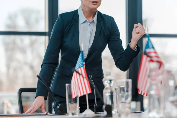 Обрізаний вид дипломата з загорнутим кулаком, що говорить, стоячи біля мікрофона та американських прапорів — стокове фото