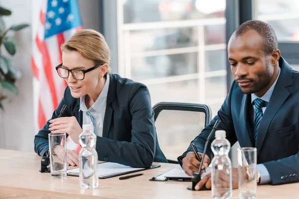 Attractive diplomat talking in microphone near african american representative — Stock Photo