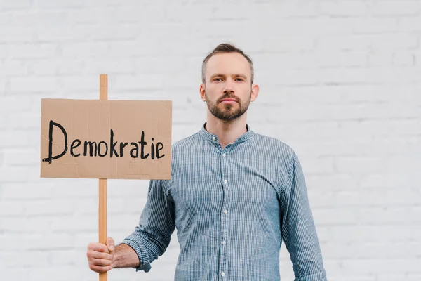 Bearded citizen holding placard with demokratie lettering near brick wall — Stock Photo