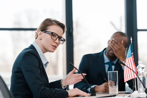 Selective focus of woman talking in microphone near african american man covering face — Stock Photo