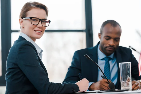 Selektiver Fokus eines glücklichen Diplomaten, der in die Kamera in der Nähe eines amerikanischen Repräsentanten blickt — Stockfoto