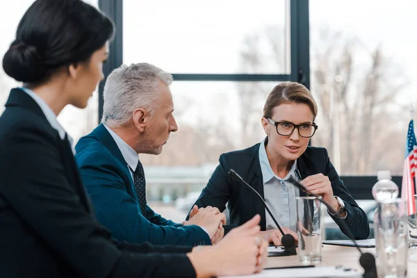 Selective focus of businesswoman talking in microphone near diplomats — Stock Photo