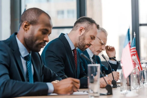 Focalizzazione selettiva dell'uomo d'affari afroamericano che scrive vicino ai diplomatici e alle bandiere dell'America — Foto stock