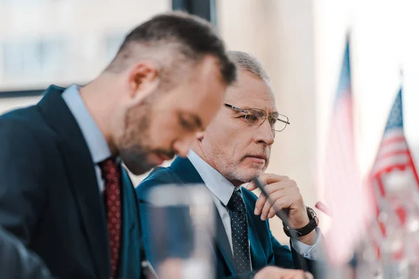 Selective focus of handsome diplomats near american flags — Stock Photo