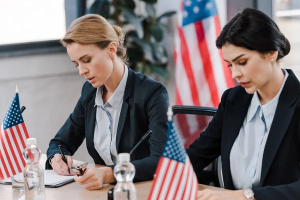 Attraente donna d'affari scrivere vicino bandiere americane — Foto stock