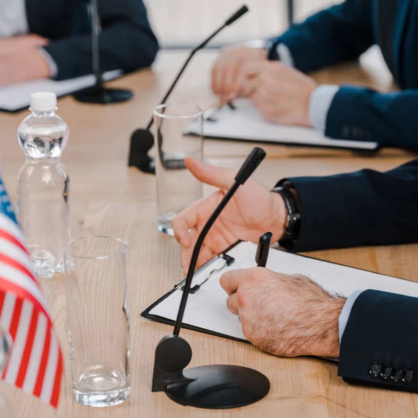 Vista recortada de diplomáticos escribiendo cerca de micrófonos y vasos en la mesa - foto de stock