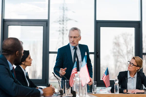 Selektiver Fokus eines bärtigen Geschäftsmannes, der mit dem Finger auf afrikanische amerikanische Diplomatin in der Nähe von Geschäftsfrauen zeigt — Stockfoto