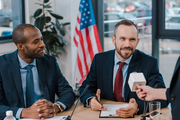 Cropped view of journalist holding microphone near happy multicultural diplomats — Stock Photo