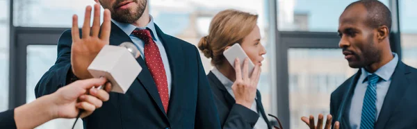 Panoramic shot of man showing no gesture near journalist with microphone and multicultural diplomats — Stock Photo