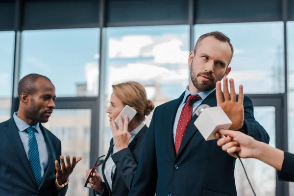 Selektiver Fokus des Geschäftsmannes, der keine Geste in der Nähe von Journalisten mit Mikrofon und multikulturellen Diplomaten zeigt — Stockfoto