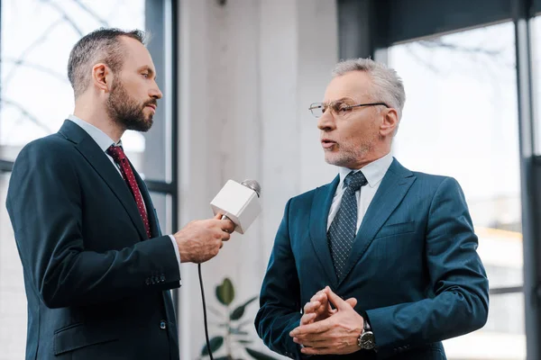 Guapo periodista sosteniendo micrófono cerca de diplomático barbudo en gafas - foto de stock