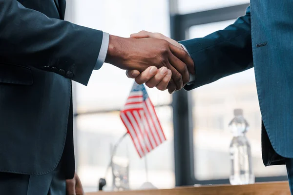Cropped view of multicultural diplomats shaking hands near flag of america — Stock Photo