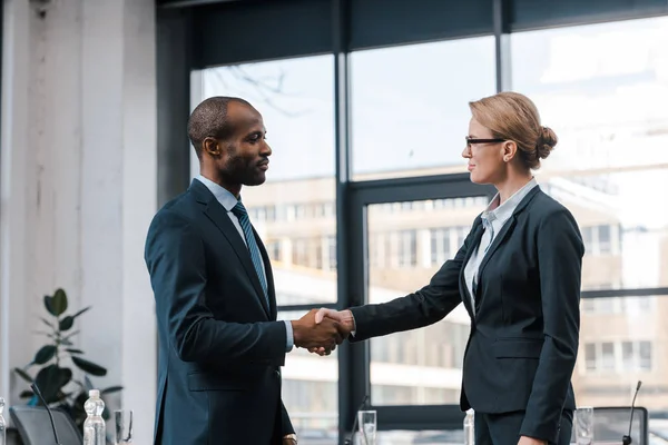 Vue de côté de femme d'affaires attrayante serrant la main avec un homme d'affaires afro-américain — Photo de stock