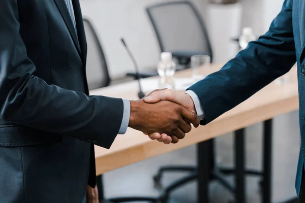 Vista recortada del hombre de negocios estrechando la mano con diplomático afroamericano - foto de stock