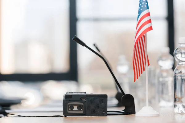 Messa a fuoco selettiva della macchina dettatura vicino al microfono e bandiera americana sul tavolo — Foto stock