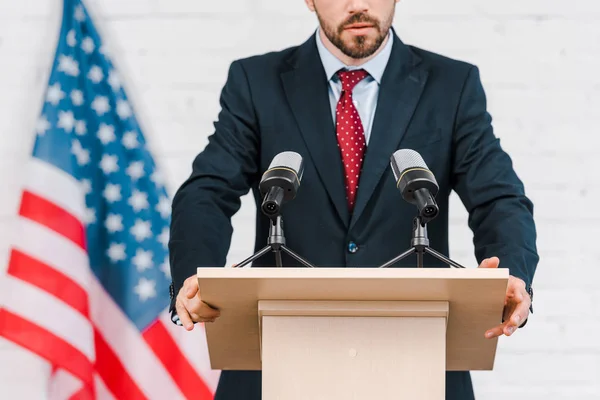 Cropped view of bearded speaker in suit standing near microphones — Stock Photo