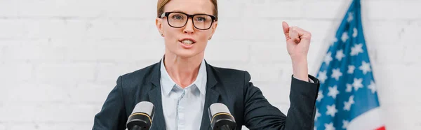 Panoramic shot of attractive speaker in glasses gesturing while talking near microphones — Stock Photo