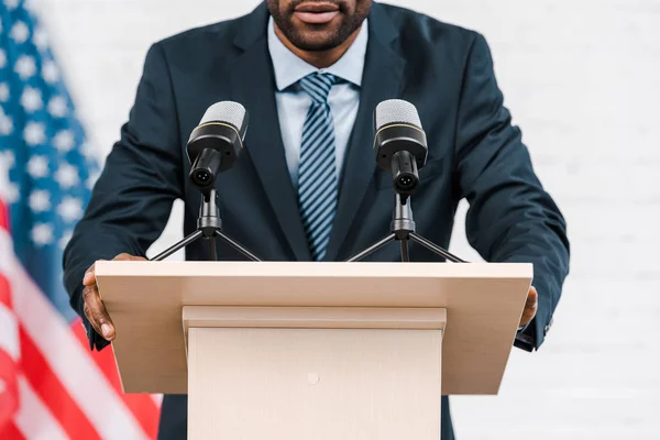 Vue recadrée de haut-parleur afro-américain parlant près des microphones et drapeau américain — Photo de stock