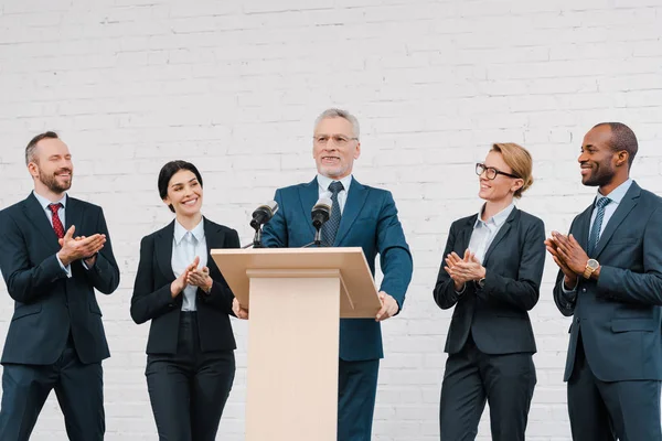 Empresarios y empresarias multiculturales aplaudiendo al portavoz barbudo - foto de stock