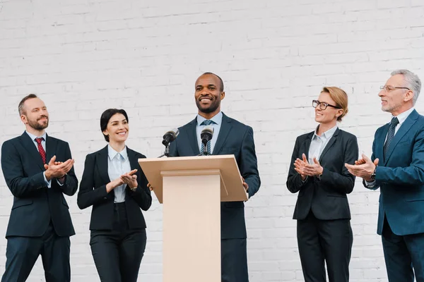 Felices hombres de negocios y mujeres de negocios aplaudiendo al portavoz afroamericano - foto de stock